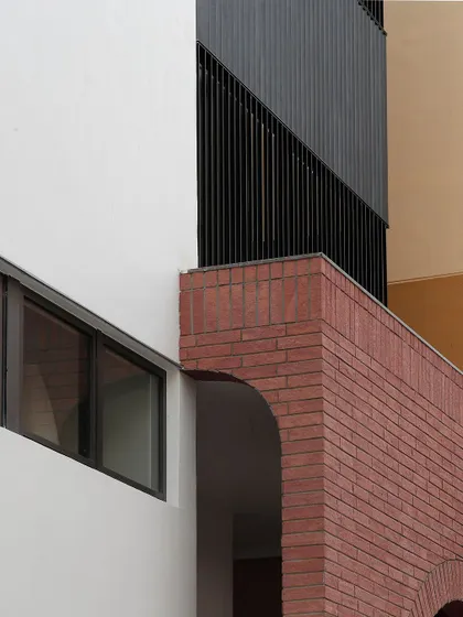 A detail shot of the Franklin Residence, showing the junction of three different materials: red brick, a black metal screen, and smooth white plaster. The clean lines and careful composition create a visually interesting architectural detail.