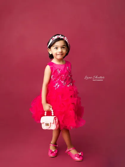A sweet, smiling portrait of a little girl in a vibrant pink dress against a matching backdrop. Simple, classic, and beautiful.