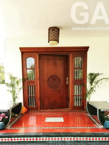An entrance that blends traditional craftsmanship with vernacular architecture. This intricately carved wooden door and red oxide flooring create a warm, ethnic welcome, grounding the home in a sense of heritage and artistry.