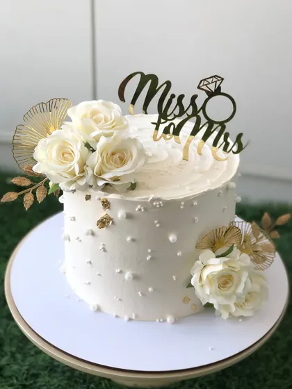 An elegant "Miss to Mrs" cake for a bridal shower, in classic white and gold with beautiful white roses.