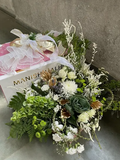 A duplicate of ID 68, this image shows a luxurious gift arrangement featuring a designer shopping bag from Manish Malhotra, overflowing with a lavish bouquet of white and green florals. This is the epitome of high-end collaborative gifting.