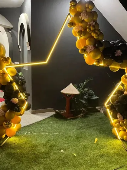 A unique star-shaped frame with black and gold balloons and LED lights. This modern and geometric design is perfect for a trendy outdoor or evening party.