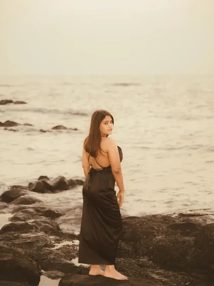 A moody, sepia-toned portrait on a rocky beach. The overcast light and the vastness of the sea create a pensive and atmospheric shot, focusing on emotion and environment.