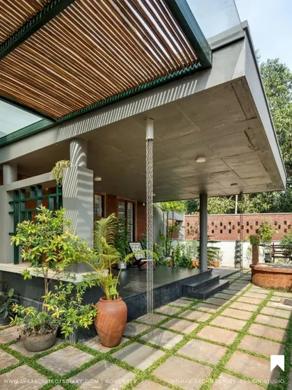 The verandah is a key part of our design philosophy, acting as a buffer between the indoors and outdoors. Here, a rain chain, potted plants, and a brick jali wall create a tranquil, shaded space.