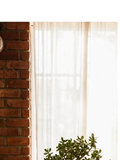 A simple, elegant light fixture on the brick wall, next to a window with sheer curtains. It's all about balancing different textures and elements.