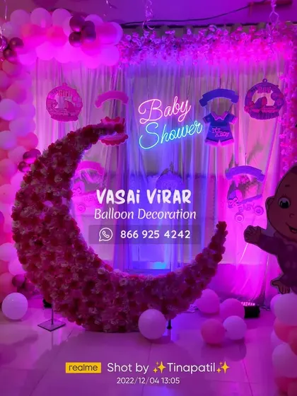 This baby shower decoration features a beautiful floral moon backdrop, perfect for photos. The setup is lit with a soft purple light and includes a "Baby Shower" neon sign and cute baby cartoon cutouts to complete the theme.