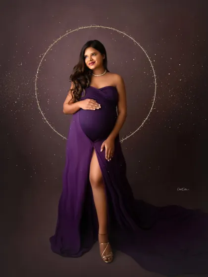 A powerful, full-length portrait. The mom-to-be stands confidently in a deep purple gown, framed by a magical golden halo.