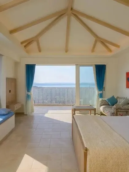 This spacious bedroom features an exposed beam vaulted ceiling and large sliding doors that open to a balcony. The design maximizes the sense of space and connection to the outdoors, with a built-in window seat for enjoying the view.