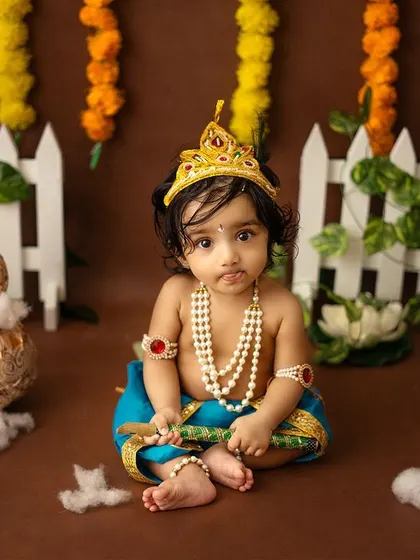 A curious little Krishna looking at the camera, surrounded by traditional props.