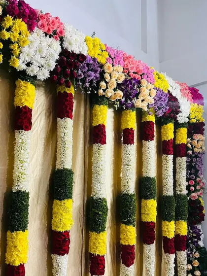 A close-up of a colorful floral garland used for stage or entrance decoration. I use a variety of fresh flowers like roses, chrysanthemums, and jasmine to create these thick, vibrant arrangements.