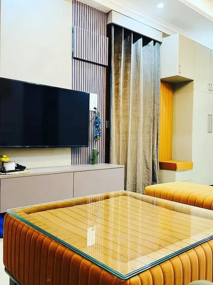 The living area in Jasola features a vibrant orange upholstered ottoman and seating, adding a playful and energetic touch to the room.