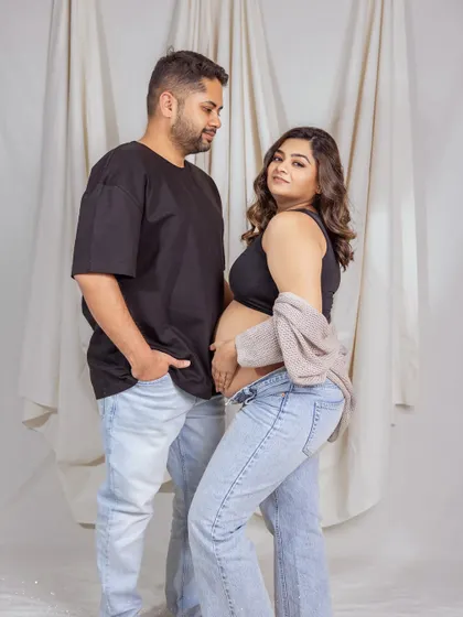 A playful and confident pose during a casual maternity shoot. The mother-to-be looks over her shoulder at the camera, her hand on her hip, while her partner looks on with a smile.