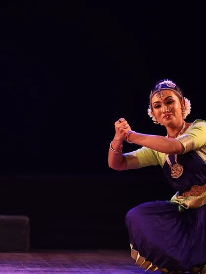 A dancer in a graceful kneeling pose, her expression full of devotion, captured during the Sadhana Classical Dance Festival.