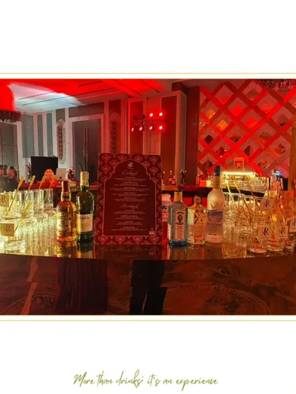 A wide view of a luxurious bar with a mirrored gold finish and dramatic red uplighting. The setup includes a custom menu and personalized glassware, reflecting the event's grand scale.