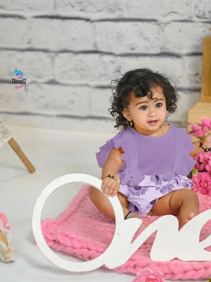 A sweet first birthday photo with a 'One' sign and a lovely pink and purple theme.