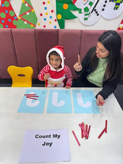 Success and a smile. This student in a Santa suit has correctly matched the number of sticks to the numeral, showing the pride that comes with mastering a new skill.