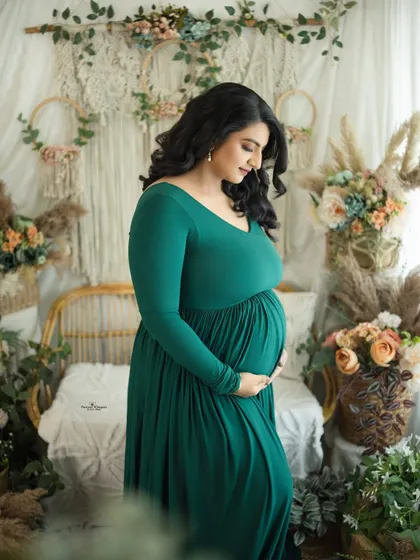 A classic side-profile portrait in a stunning emerald green gown. This pose beautifully highlights the baby bump against our earthy boho backdrop.