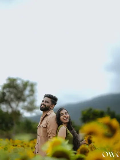 A playful back-to-back pose in a sunflower field, capturing the couple's joyful interaction during their pre-wedding shoot.