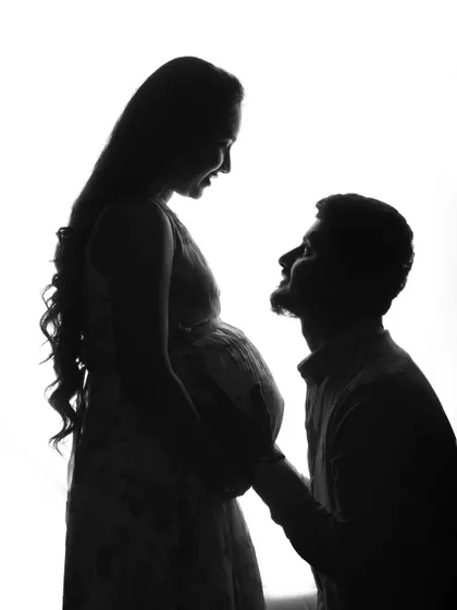 A tender silhouette of a partner kneeling to connect with the baby bump. This black and white photo is full of emotion, capturing a quiet moment of anticipation and love.
