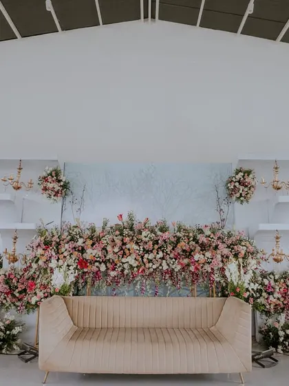 This stage design showcases a symphony of flowers against a clean, modern backdrop. The arrangement flows organically across different levels, creating a sense of depth and luxury, complemented by small chandeliers.