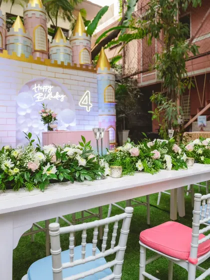 A long shot of a princess party dining setup, featuring a castle backdrop and a beautifully decorated table with a floral runner. I can transform any space, even a backyard, into a royal banquet hall.