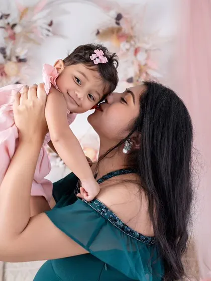 A mother lifts her daughter up for a sweet kiss on the cheek. The baby's happy expression and the mother's loving gesture make this a heartwarming photo.