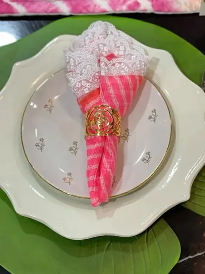Uplift your table decor with the charm of colorful napkins. Here, a bright pink and white napkin is paired with an elegant gold ring, creating a beautiful balance of color and sophistication.