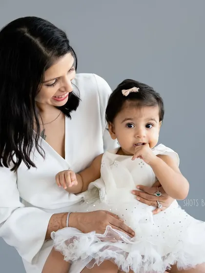 A classic and elegant mother daughter portrait. The simple grey background and white outfits create a timeless and sophisticated look.
