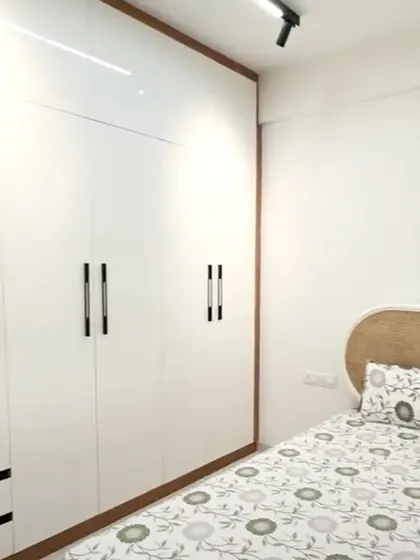 A clean and minimalist bedroom with a white floor-to-ceiling wardrobe. The simple design with sleek black handles is framed with wood, adding a touch of warmth to the modern aesthetic.