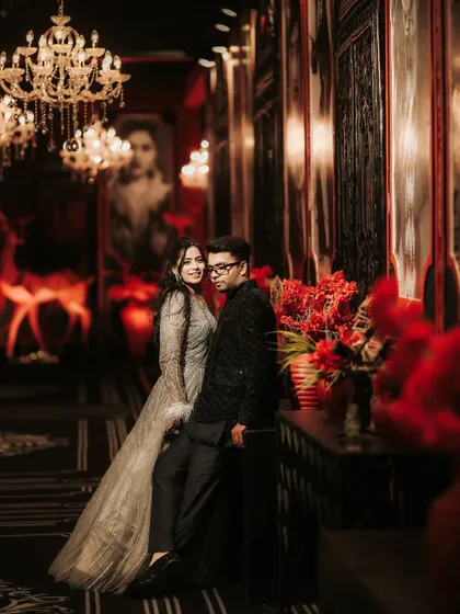 A stylish and moody portrait of the couple at their Sangeet. The opulent setting with chandeliers and rich red decor provides a dramatic backdrop for this elegant and romantic photograph.