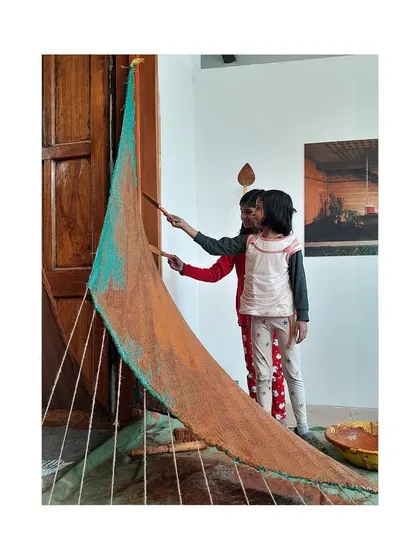 A duplicate image showing children engaging with the interactive mud plastering exhibit at the biennale.