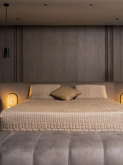 Minimalism meets warmth in this bespoke bedroom. A low-profile bed is framed by a dark, textured headboard wall, with integrated LED lighting casting a subtle glow that highlights the rich materiality and creates an intimate atmosphere.