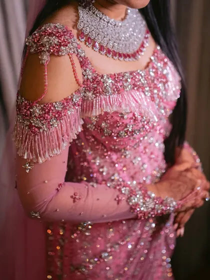 A close up of the cold shoulder detail on a modern bridal gown. Cascading beadwork and shimmering tassels add movement and a touch of playful glamour to the structured bodice.