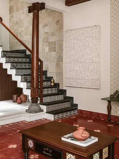 The staircase in 'Project Varnika' is a work of art, with mosaic-clad risers and traditional Athangudi floor tiles. An antique wooden pillar anchors the space, reinforcing the home's heritage theme.