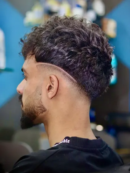 Fade today, confidence forever. This curly haircut is enhanced with a sharp, curved razor line that adds a dynamic element to the style.