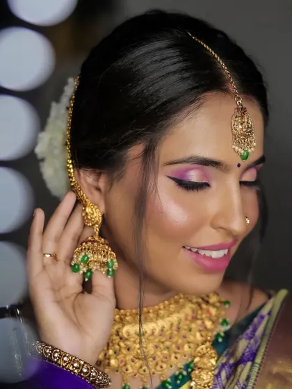 A close-up portrait focusing on the bride's beautiful gold jhumkas. Her smile and the soft focus background with bokeh lights create a dreamy and joyful image.
