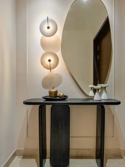 First impressions matter. This entryway console makes a statement with its sculptural black wood form and an organically shaped mirror. The wall sconces cast a soft, welcoming glow, while the minimalist decor adds a touch of artistic elegance.