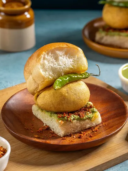A Mumbai-style Vada Pav, with a spiced potato fritter tucked inside a soft bun, layered with dry garlic chutney and green chutney.