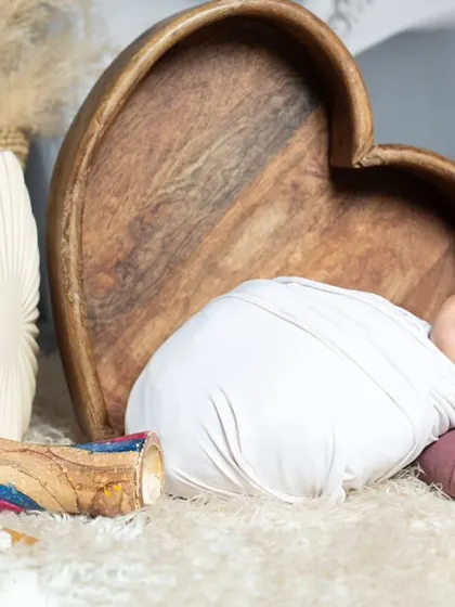 This newborn is smiling in his sleep, wrapped snugly and resting against a wooden heart prop.