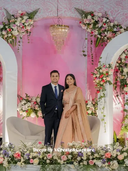 An elegant reception stage with white arches, pastel pink backdrop, and beautiful floral arrangements, perfect for a sophisticated evening.