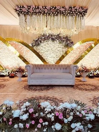 This grand reception stage uses sweeping, curved backdrops covered in thousands of flowers. The hanging floral chandelier and intricate floor patterns complete this luxurious and impressive design.