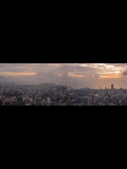 A letterboxed panoramic view of the Mumbai cityscape, emphasizing the wide, cloudy sky above.