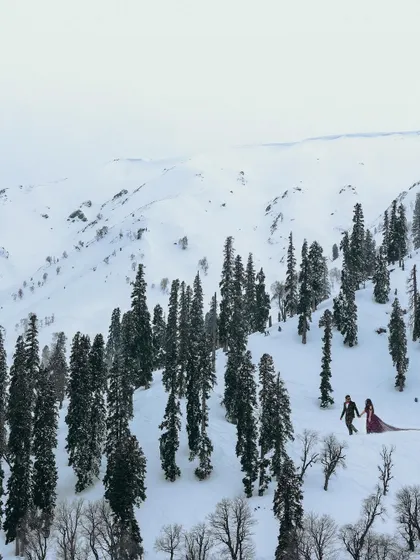 A wide, breathtaking shot showing the couple walking through a vast, snowy valley in Kashmir, emphasizing the grand scale of their love story.