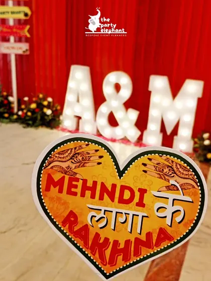 Another fun photo prop, this one shaped like a heart with the phrase 'Mehndi Laga ke Rakhna', set against the backdrop of the couple's marquee initials.