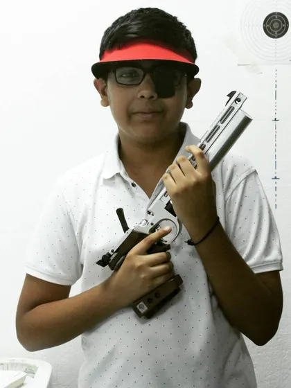 A young student proudly holds his air pistol after a successful practice session. Building confidence is one of the key benefits of learning to shoot.