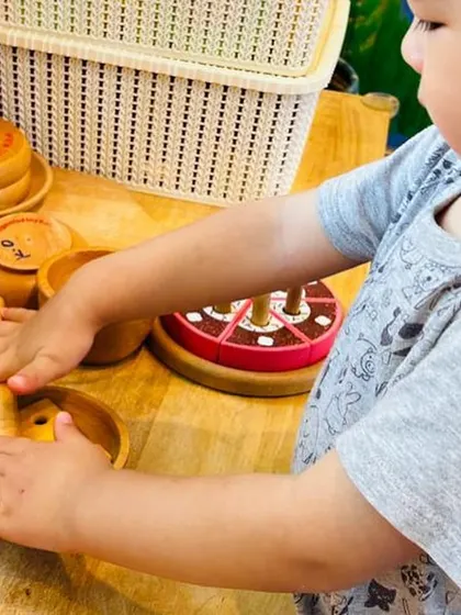Our role-play zone is a favorite! Here, a child explores wooden kitchen toys, pretending to cook and prepare food.
