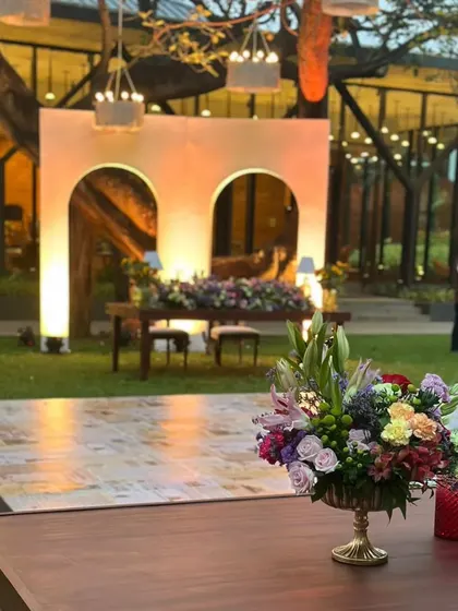 A view of the sweetheart table set against a custom-built arched backdrop, with the beautiful garden and glasshouse venue in the background.