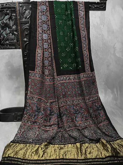 A sophisticated black and green Ajrakh saree with a gold border. This piece combines the earthy beauty of block prints with a touch of festive glamour.