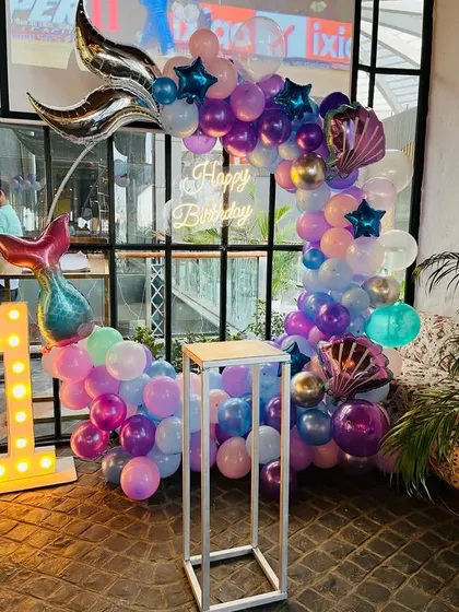 An enchanting mermaid theme for a first birthday. The balloon arch in shades of purple and blue is accented with a large mermaid tail foil balloon and a light-up number '1'.