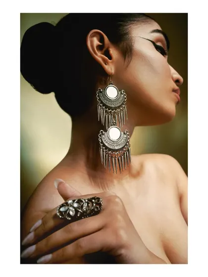A classic beauty portrait highlighting large, ornate silver earrings. The soft, warm light on the model's skin contrasts beautifully with the cool tone of the metal jewelry.